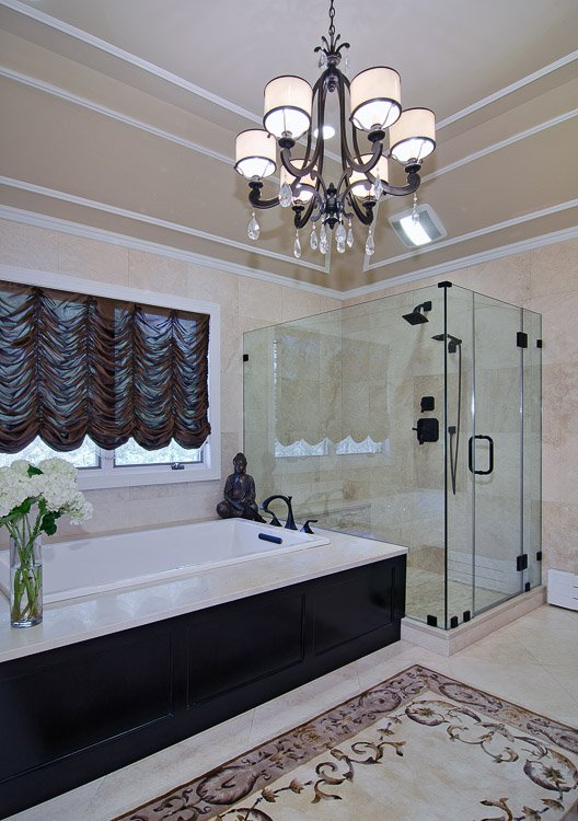 Large soaker tub with chandelier above and a glass shower
