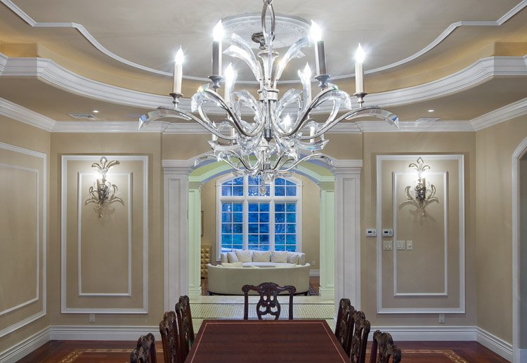 Dining room with wood table, chandelier and wall sconces looking into a living room with a large window