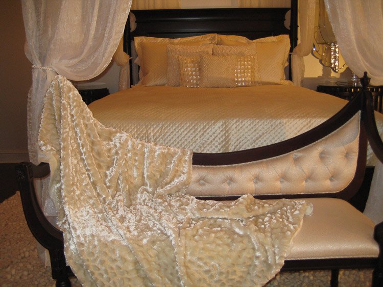Wooden bedframe with white linens and lots of pillows and a bench at the foot of the bed