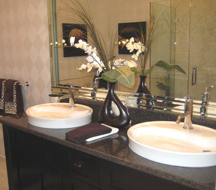 Bathroom vanity with dark countertop and dual white sinks with a mirror, towels and orchid