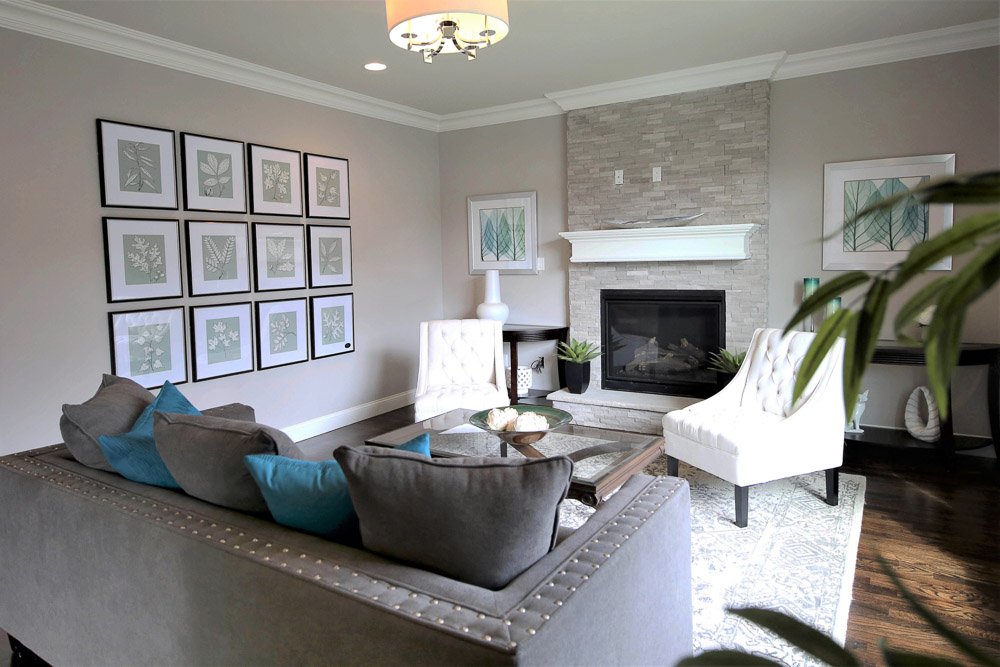Living area with grey couch, two white chairs, fireplace with mantle and art on the walls