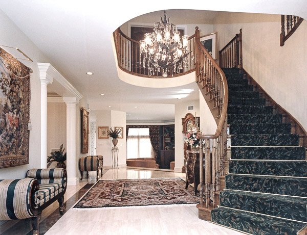 Foyer with grand carpeted staircase, chandelier, area rug and two setees