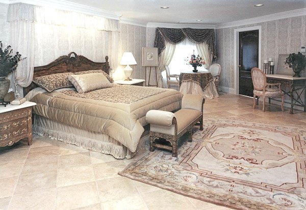 Large bedroom with a bed, table and 2 chairs, makeup vanity and chair, bench and two night tables and a rug
